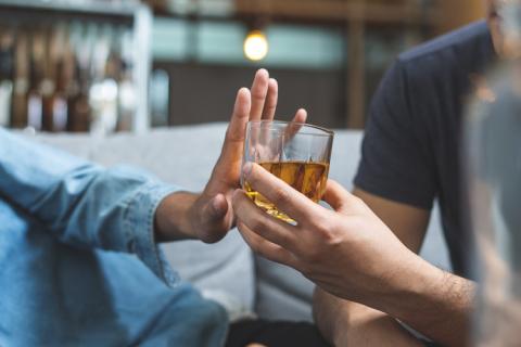 Persona con intolerancia al alcohol rechazando con la mano un vaso de licor